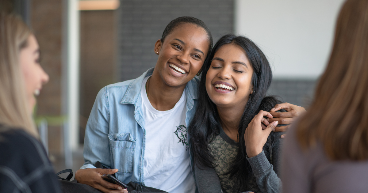 Two women sitting together with their arms around each other. The image shows the impact of support in the recovery journey.