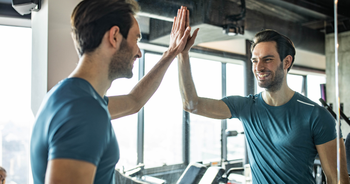 Man smiling and giving himself a high-five in the mirror at the gym, celebrating progress and commitment to his recovery journey.